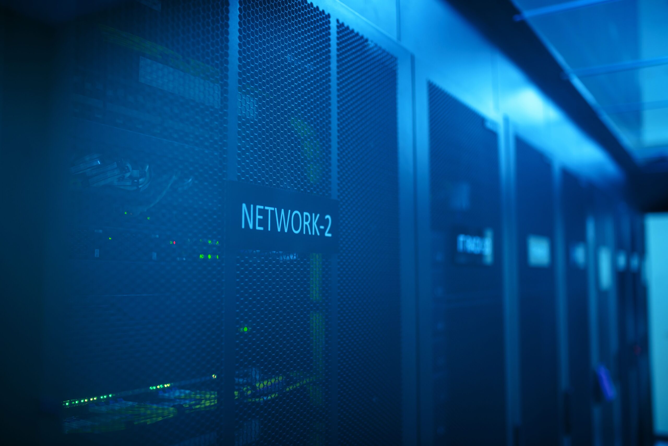 Een serverruimte met blauwe verlichting, KLAAR-racks met het opschrift „NETWORK-2“ en zichtbare apparatuur voor webhosting.